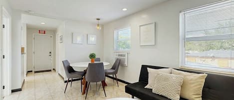 A modern interior with a dining area, a sofa, and a window with blinds.