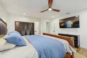 A bedroom with a bed, a ceiling fan, a television, and a wardrobe. - The Sunshine Hideaway (Wilton Manors)