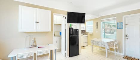 A compact kitchen with white cabinets, a black refrigerator, and a dining area with a white table and chairs.