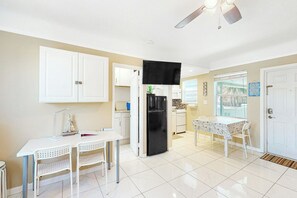 A compact kitchen with white cabinets, a black refrigerator, and a dining area with a white table and chairs. - Eternal Coastal Sunshine (Hollywood)