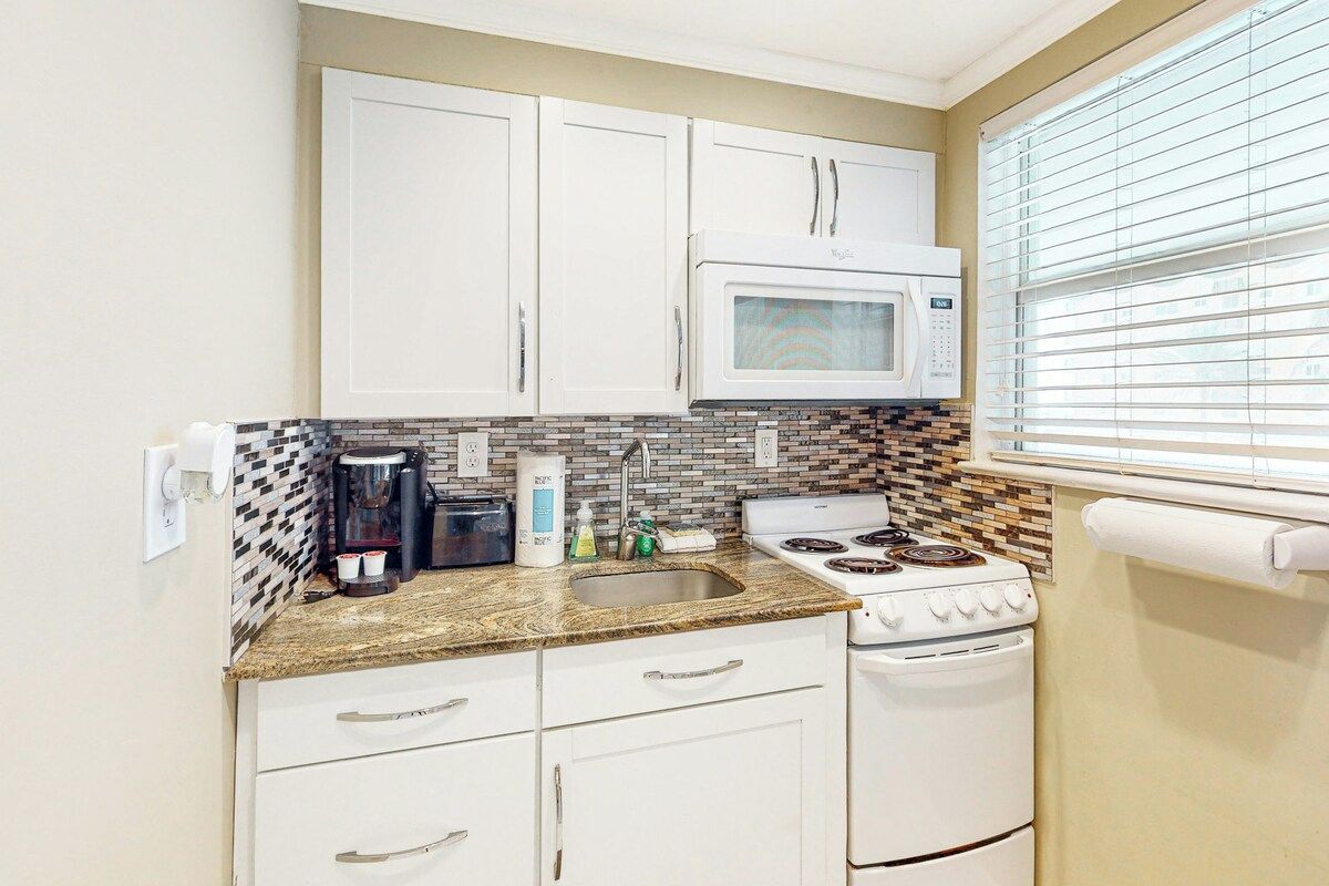 Cocina compacta con armarios blancos, microondas, estufa y fregadero.