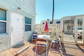 A residential building with a white door marked with the number 9, a small patio with a table and chairs, and a white fence with cut-out patterns. - Eternal Coastal Sunshine (Hollywood)