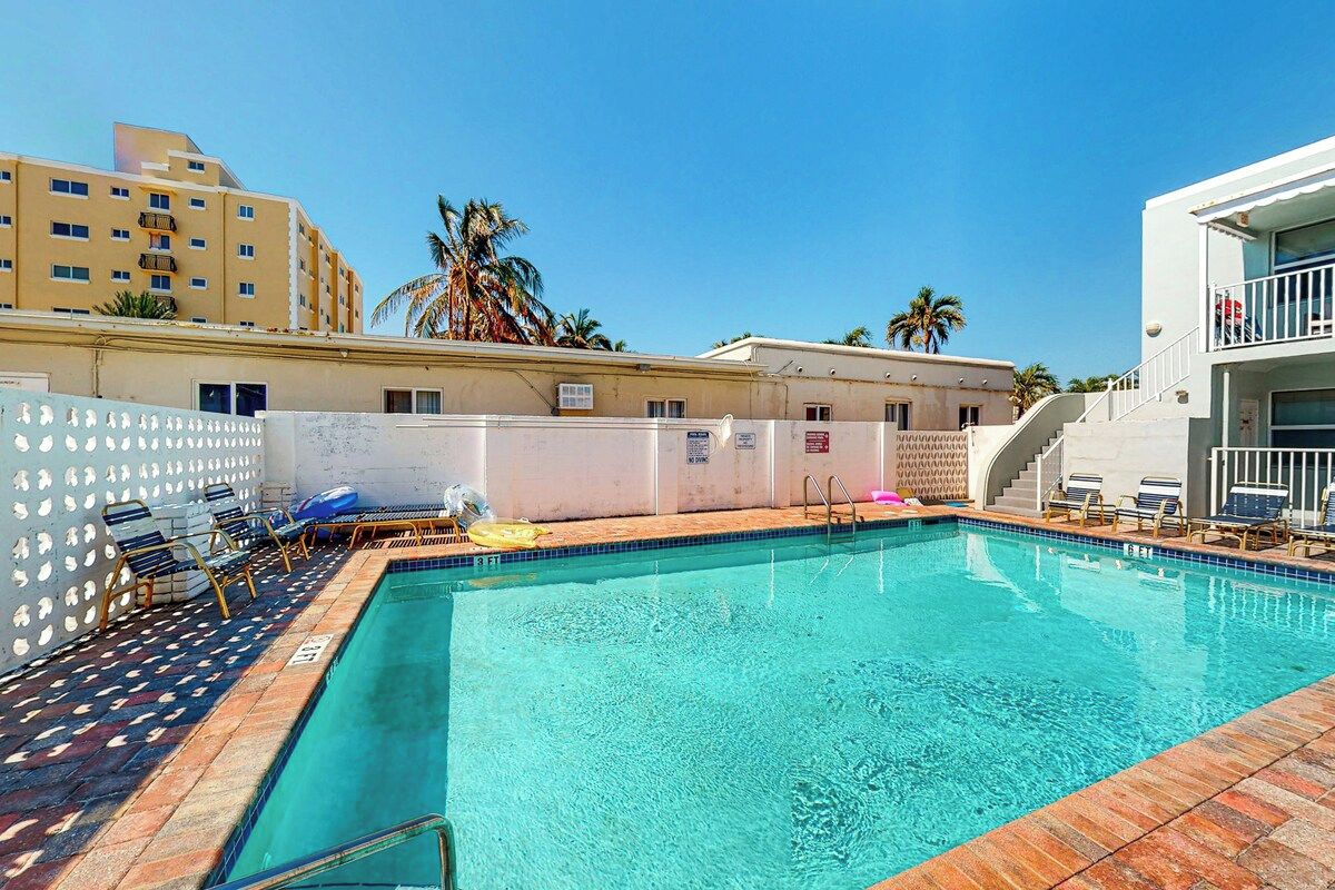 A swimming pool with lounge chairs and a white fence.
