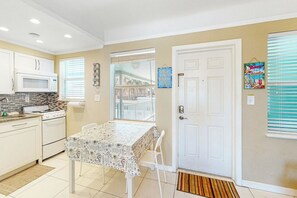 A kitchen with white cabinets, a microwave, a stove, and a dining table with a patterned tablecloth. - Eternal Coastal Sunshine (Hollywood)