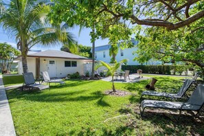 Una propietat residencial amb un jardí ben cuidat, zona d'estar a l'exterior i un edifici petit amb una porta i finestres.