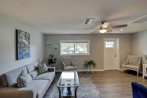 A spacious living room with a sofa, a glass coffee table, and two striped armchairs. - Coconut Grove Singer Island - Unit 1 (Riviera Beach)