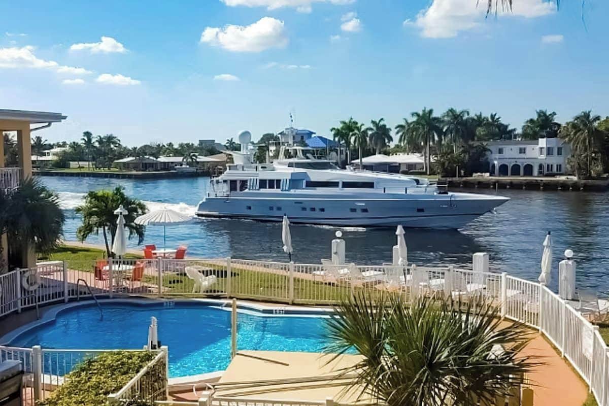 Eine große Yacht liegt an einem Pool mit Blick auf das Wasser und Palmen.