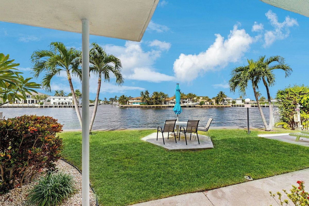 A patio with a view of a body of water, palm trees, and a distant building.