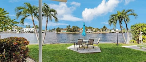 A patio with a view of a body of water, palm trees, and a distant building.