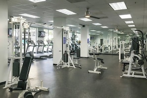 Uma academia com diversos equipamentos de exercício, espelhos e esteira.