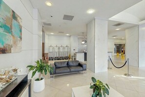 A modern hotel lobby with a reception desk, a sofa, and potted plants. - The Ocean Reserve 1607 (Sunny Isles Beach)