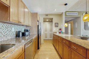 A kitchen with wooden cabinets, a tiled backsplash, a stainless steel sink, and a refrigerator. - The Ocean Reserve 1607 (Sunny Isles Beach)