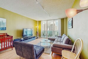 A living room with a television, sofa, and a red crib. - The Ocean Reserve 1607 (Sunny Isles Beach)