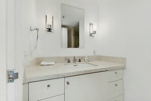 A bathroom with a white sink, two faucets, a mirror, and two wall-mounted light fixtures. - The Carlyle 3G - Near Beach (Miami Beach)