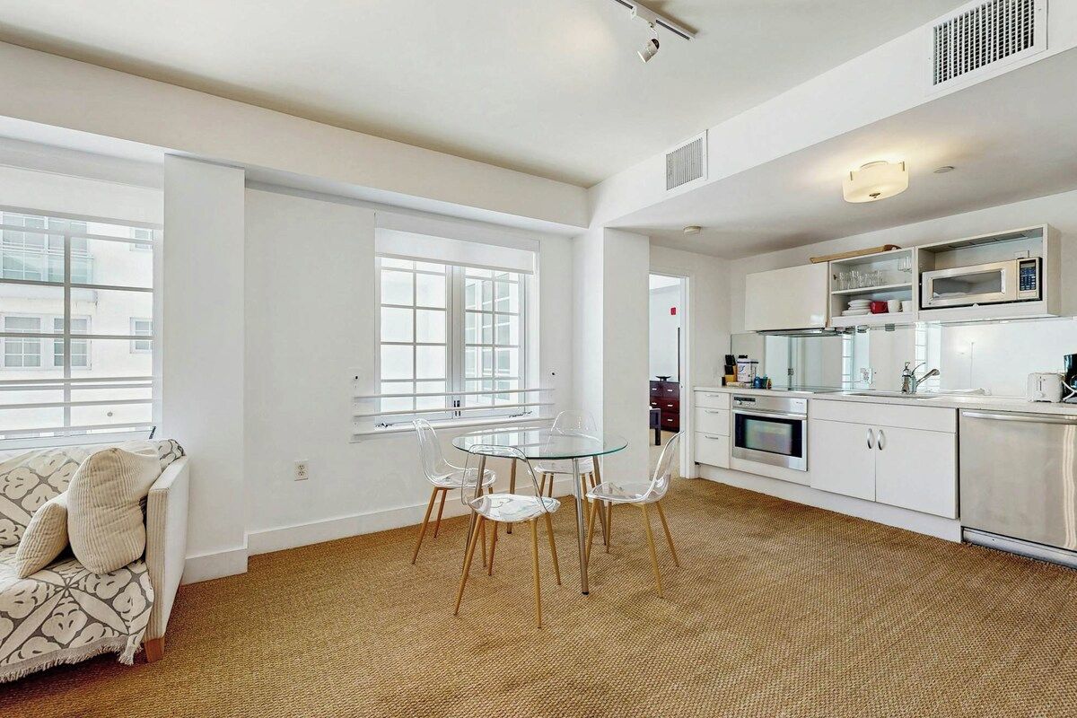 A modern kitchen with white cabinetry, stainless steel appliances, and a glass dining table with chairs.