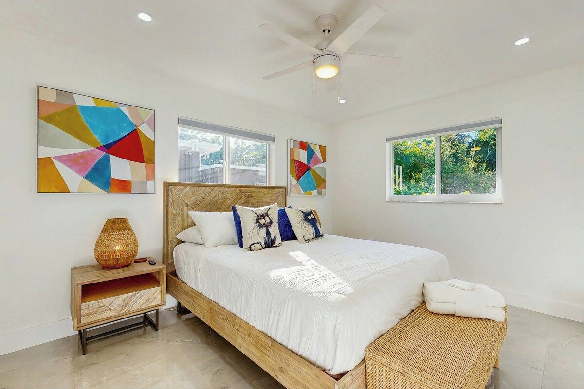 A modern bedroom with a wooden bed, white bedding, and geometric wall art.