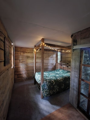 Una habitación tipo cabaña de madera con una cama con dosel, luces de adorno y una ventana.