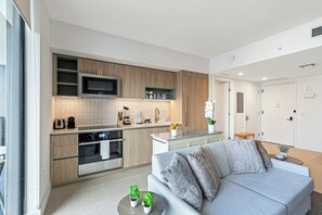 A modern kitchen with built-in appliances and a grey sofa in the living area. - The Grand Vista 4501 (Miami)
