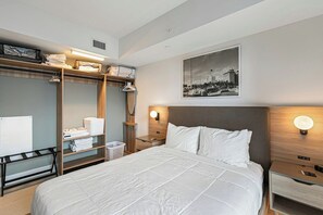 A hotel room with a bed, a wardrobe, a nightstand, a wall-mounted light, and a framed picture. - The Grand Vista 4501 (Miami)