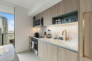 Cozinha moderna com micro-ondas embutido, pia com torneira dourada e janela com vista para a paisagem urbana.