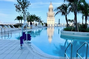 A swimming pool with a reflection of a tower, surrounded by palm trees and lounge chairs. - The Grand Vista 4501 (Miami)