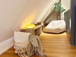 Ein gemütliches Schlafzimmer im Loft-Stil mit schrägem Dach, einem Nachttisch mit Lampe, einem Korbstuhl und einem Sitzsack.