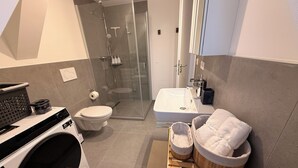 A modern bathroom with a glass-enclosed shower, a white sink, and a wooden laundry basket with towels. - A Hidden Gem in the Heart of Ingolstadt (Ingolstadt)