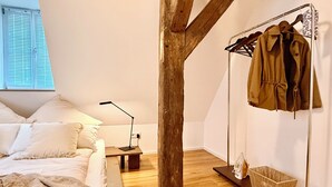 Un dormitori amb llit, taula de nit, làmpada i un penjador amb un abric.