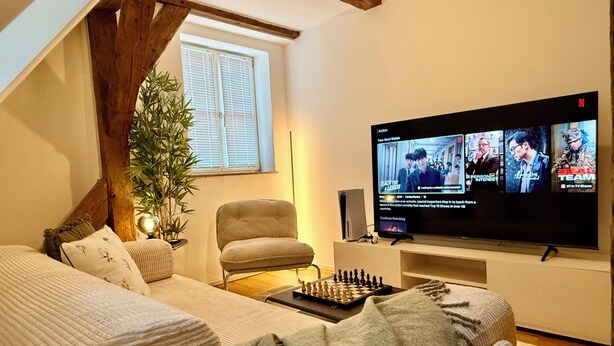 Una habitació acollidora amb un llit, una cadira, un televisor i un tauler d'escacs.
