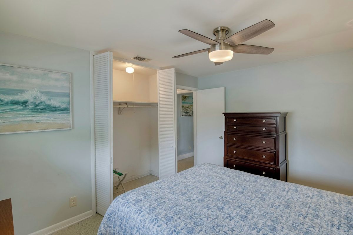 A bedroom with a bed, a ceiling fan, a dresser, and a closet.