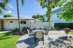 A patio with a round table and chairs, a grill, and a white fence. - Coconut Grove Singer Island - Units 1, 3, & 4 (West Palm Beach)