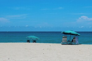 A beach with two umbrellas and chairs, a clear sky, and the ocean in the background. - Coconut Grove Singer Island - Units 1, 3, & 4 (West Palm Beach)