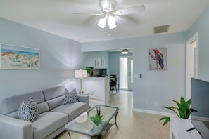 A living room with a grey sofa, a glass coffee table, a ceiling fan, and artwork on the walls. - Coconut Grove Singer Island - Units 1, 3, & 4 (West Palm Beach)