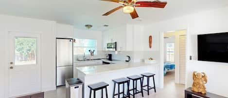 A modern kitchen with a central island, bar stools, a ceiling fan, and a TV mounted on the wall.