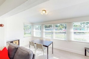 Een lichte kamer met een eettafel, stoelen en een raam met jaloezieën.