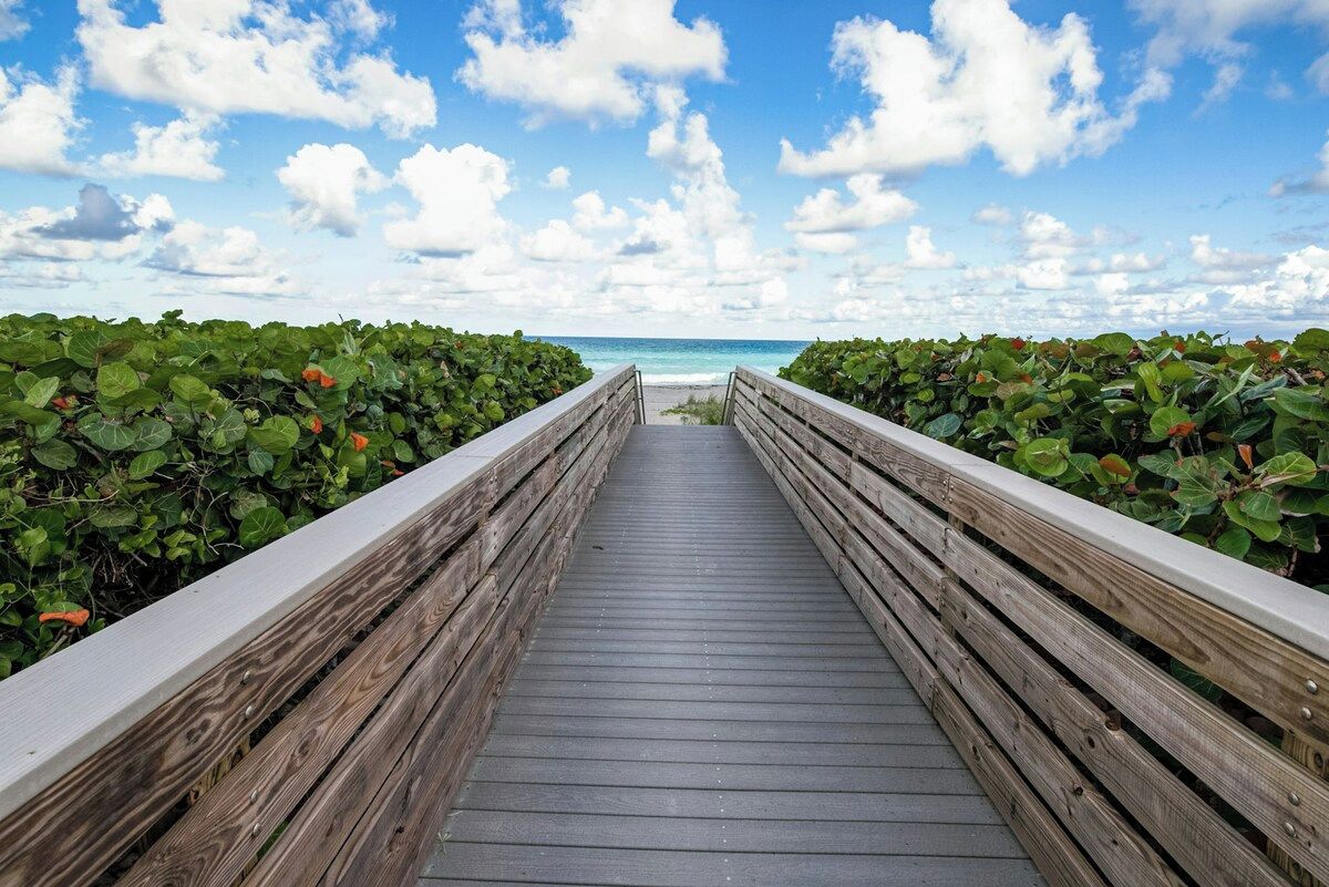 A wooden boardwalk leading to a beach with a clear sky and clouds.