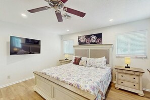 Ein Schlafzimmer mit einem Bett, Nachttischen, einem Deckenventilator, einem Gemälde und einem Fenster mit Jalousien.