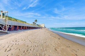 Ein Strand mit einem Betonweg, Fußabdrücken und blauem Himmel.