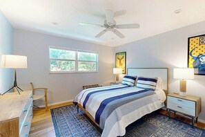 Ein Schlafzimmer mit einem Bett, Nachttischen, einem Schreibtisch, einem Stuhl, einem Fenster und einem Deckenventilator.