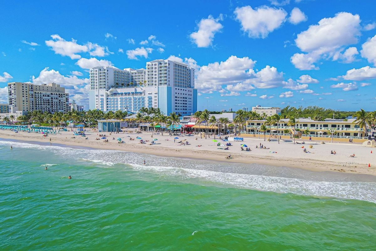A beachfront hotel with multiple high-rise buildings, a sandy beach, and palm trees.