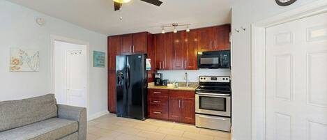A compact kitchen with a refrigerator, microwave, stove, and ceiling fan.
