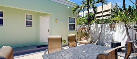 An outdoor patio with a table and chairs, a door, and a white fence.