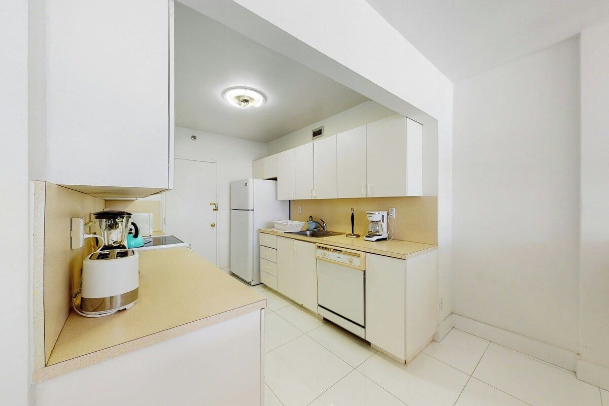 A compact kitchen with white cabinets, a toaster, a coffee maker, and a dishwasher.