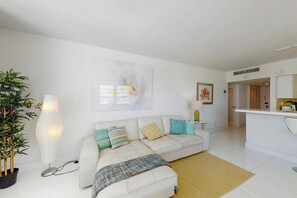 Ein modernes Wohnzimmer mit einem weißen Sofa, einer gemusterten Decke und einem großen abstrakten Gemälde.