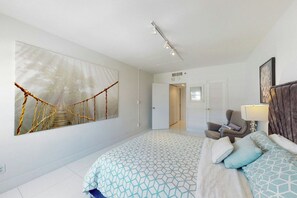 Quarto com cama, poltrona, escrivaninha e uma grande obra de arte na parede retratando uma ponte de corda.