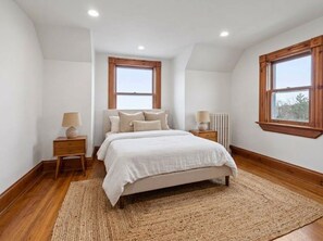 Une chambre à coucher avec un lit, deux tables de chevet, un radiateur et deux fenêtres.