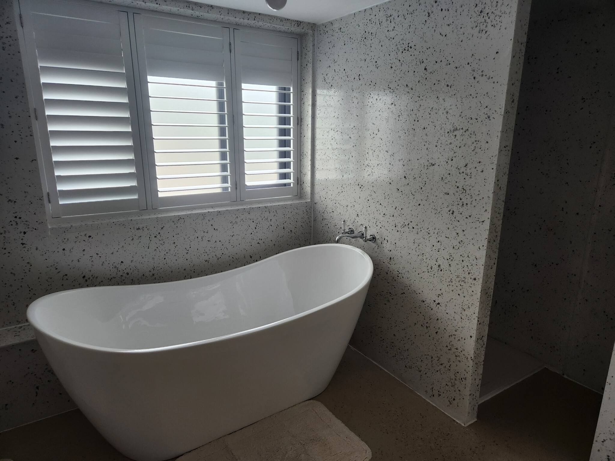 Une salle de bain avec une baignoire sur pieds, une fenêtre avec des stores et des murs à motifs.