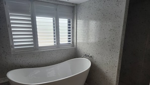 A bathroom with a freestanding bathtub, a window with blinds, and speckled walls. - The Pigsty at the Secret Garden (Ashford)