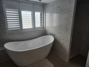 A bathroom with a freestanding bathtub, a window with blinds, and speckled walls. - The Pigsty at the Secret Garden (Ashford)