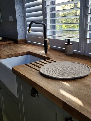 A kitchen with a wooden countertop, a sink with a black faucet, and a window with blinds.